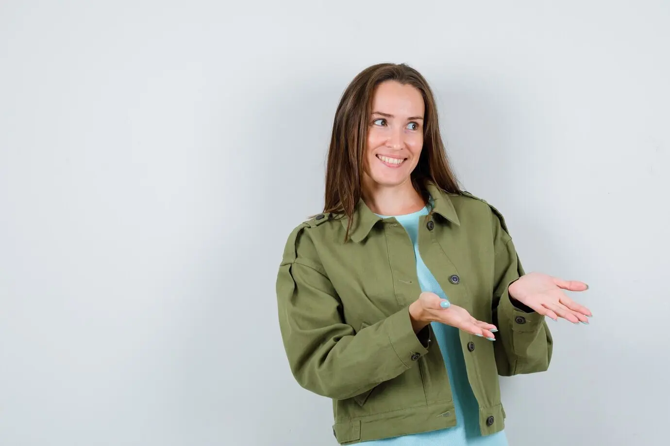 Frontalansicht einer jungen Dame in grüner Jacke, die gestikuliert und fröhlich wirkt.
