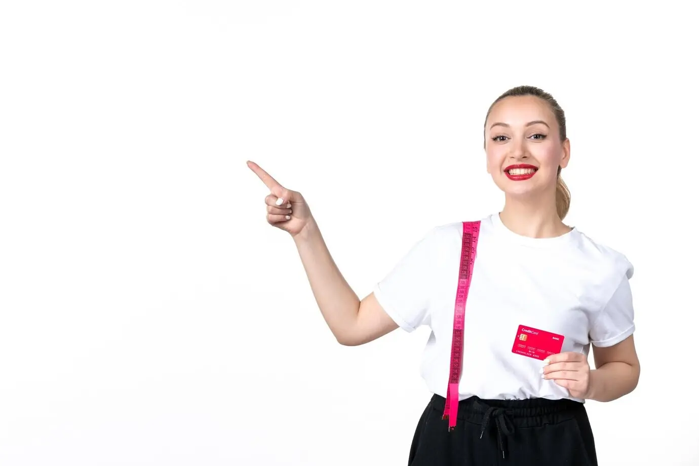 Vorderansicht einer jungen Frau mit Maßband und Kreditkarte vor weißem Hintergrund, verliert an Hautschönheit, misst den schlanker werdenden Körper, die Hüfte und den Oberkörper; Geld, Bank.